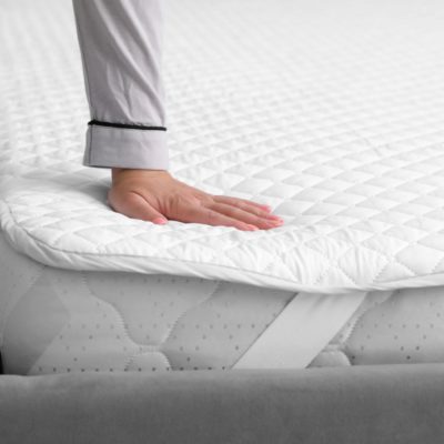 Quilted mattress topper with elastic anchor bands on all corners, lightweight and breathable design with a soft cotton cover, shown on a neatly made bed
